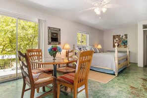 A bedroom with a bed, a dining table with chairs, a ceiling fan, and a window with a view of trees. - Casa del Rio | Pet-Friendly River Stay with Views (Bandera)