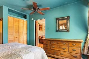 A bedroom with a bed, wooden dresser, ceiling fan, and a mirror on the wall. - Casa del Rio | Pet-Friendly River Stay with Views (Bandera)