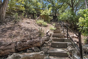 A stone staircase leading uphill with metal railings, surrounded by trees and rocky terrain. - Casa del Rio | Pet-Friendly River Stay with Views (Bandera)