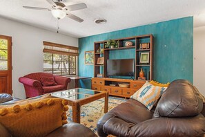 A living room with a television, a red armchair, a brown leather sofa, and a coffee table. - Casa del Rio | Pet-Friendly River Stay with Views (Bandera)