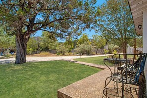 A well-maintained outdoor area with a lawn, a metal table and chairs, and a large tree. - Casa del Rio | Pet-Friendly River Stay with Views (Bandera)