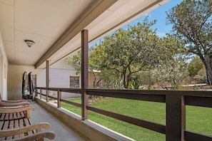 A covered outdoor area with a wooden bench, a railing, and a view of a grassy yard with trees. - Casa del Rio | Pet-Friendly River Stay with Views (Bandera)