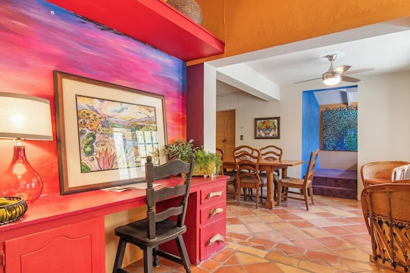 A dining area with a red wall, a framed painting, and a ceiling fan.