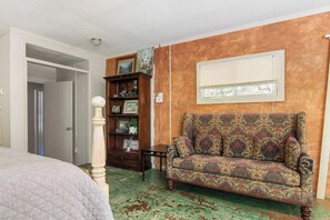 Een kamer met een gestreept sofa, een houten boekenkast, een deur naar een andere kamer en een raam met zonwering.