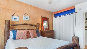 Una habitación con una cama, cabecera de madera, una mesita de noche, un espejo y una cortina.