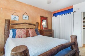 Een kamer met een bed, een houten hoofdeinde, een nachtkastje, een spiegel en een gordijn.