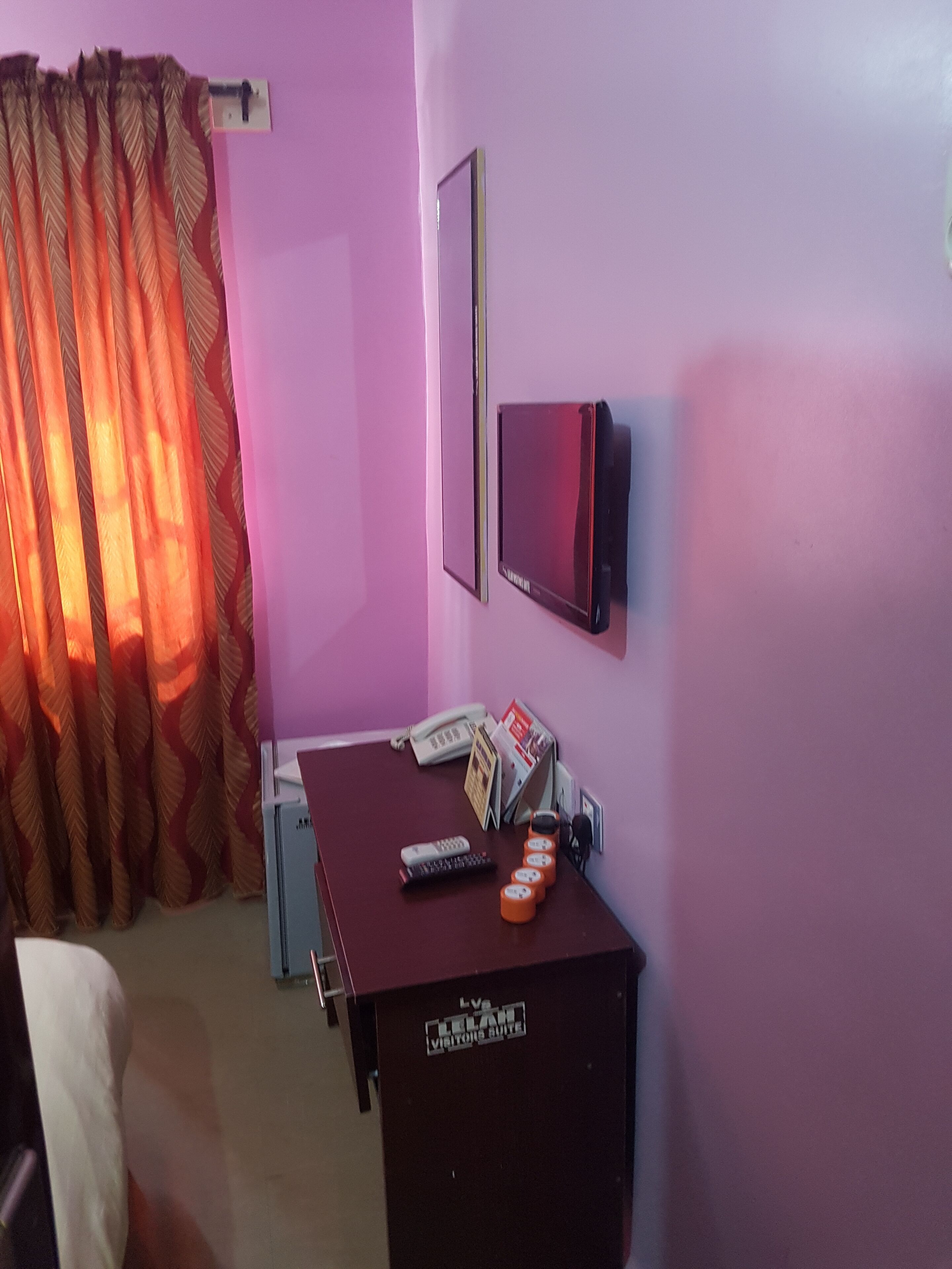 A room with a desk, a telephone, a TV, and a curtain.