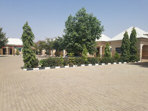 A paved courtyard with a building featuring a tiled roof and columns. - Lelah Visitors Suite (Gombe)