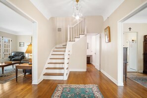 A staircase leading to a second floor, a living room with a leather chair, a table, and a lamp, and a kitchen area with a refrigerator. - Hacienda del Rio | Historic Home on Medina River (Bandera)