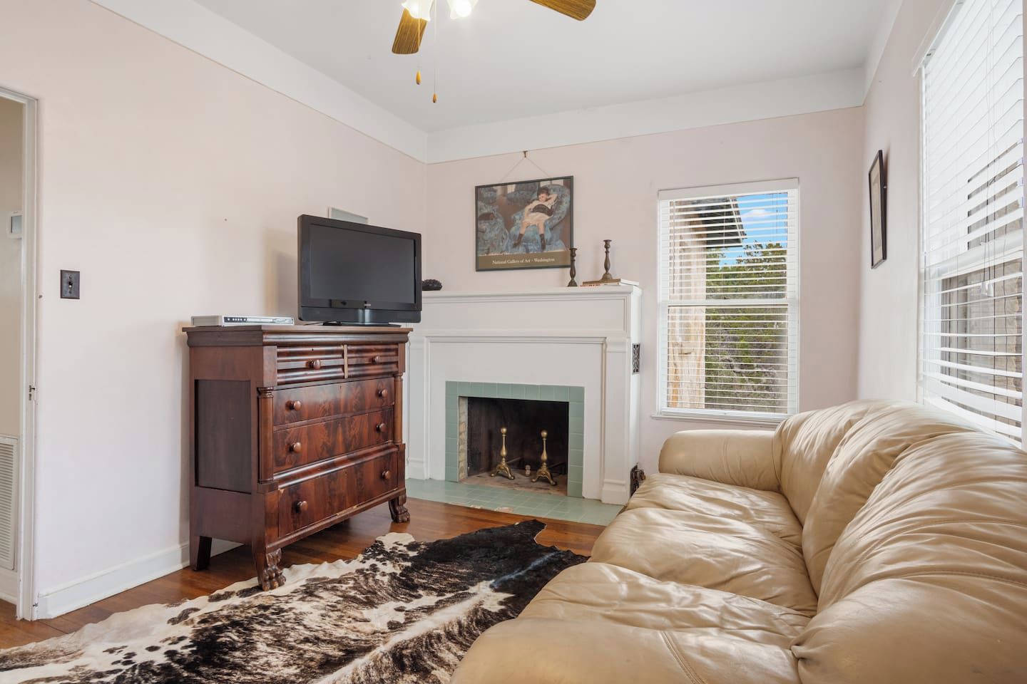 A living room with a fireplace, a television on a wooden cabinet, a leather sofa, and a cowhide rug.