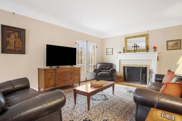 Ein Wohnzimmer mit Ledersofas, einem Holztisch, einem Fernseher, einem Kamin und einem gemusterten Teppich.
