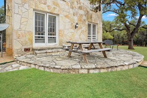 A stone building with a picnic table in the center, surrounded by a stone patio. - Hacienda del Rio | Historic Home on Medina River (Bandera)