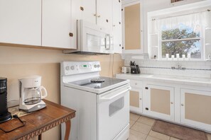 A kitchen with white cabinets, a stove, a coffee maker, and a window with a view of trees. - Hacienda del Rio | Historic Home on Medina River (Bandera)