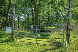 A metal gate with a warning sign indicating no vehicles beyond a certain point and a caution sign advising to swim at one's own risk. - Clear River Cabin | Secluded 2BR w/ River Access (Bandera)
