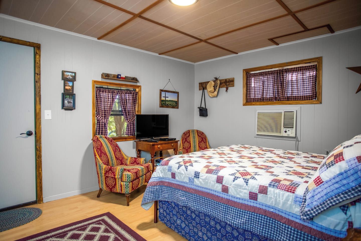A bedroom with a bed, a chair, a television, and a window with curtains.