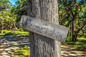A wooden sign attached to a tree in a wooded area. - Clear River Cabin | Secluded 2BR w/ River Access (Bandera)