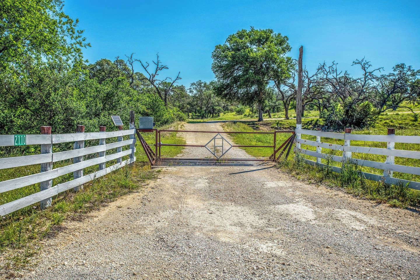 A gravel path leading to a gated entrance with a white fence and a gate.