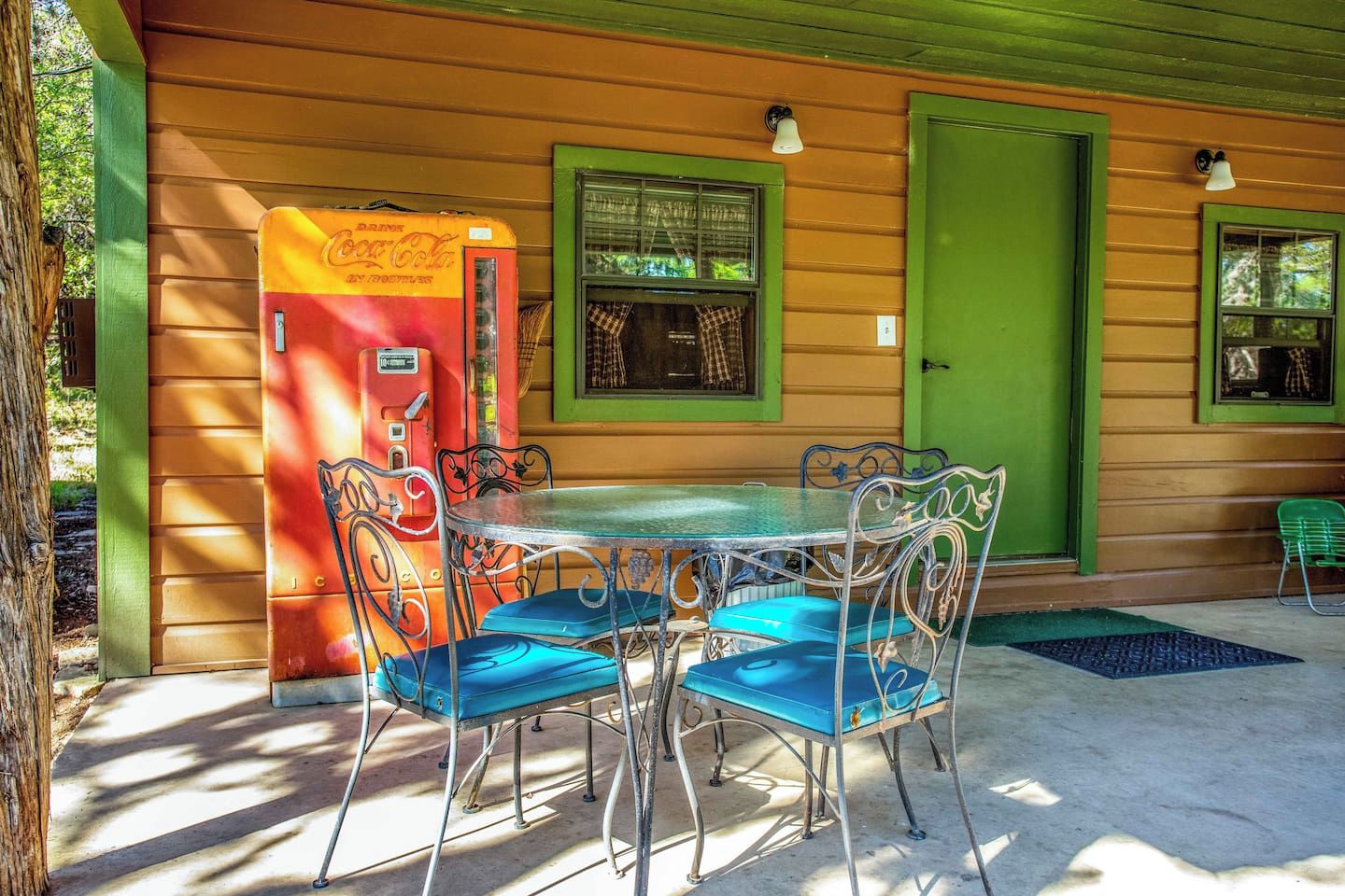 A dining area with a table and chairs, a vintage Coca-Cola vending machine, and a green door.