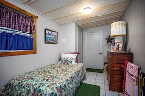 A bedroom with a bed, a dresser, a lamp, and a door. - Clear River Cabin | Secluded 2BR w/ River Access (Bandera)