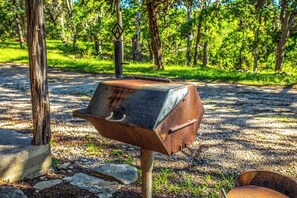 A rusty barbecue grill in a wooded area. - Clear River Cabin | Secluded 2BR w/ River Access (Bandera)