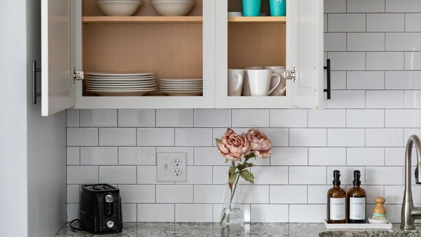 Cucina con mobili bianchi, un piano di lavoro in marmo, un tostapane, un vaso con fiori e flaconi di detersivo per piatti.