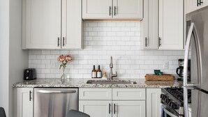 Una cucina moderna con mobili bianchi, un piano di lavoro in granito, un frigorifero in acciaio inox e un forno integrato.