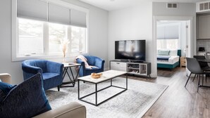 Un soggiorno moderno con televisione, poltrone blu, un tavolino da caffè e un'area cucina sullo sfondo.