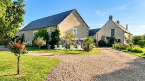 A two-story house with a gravel driveway, a lawn, and a small tree with red flowers. - Homerez - Studio in Thilouze (Thilouze)