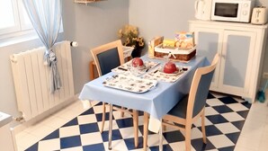 A dining area with a checkered floor, a table set with plates and glasses, chairs, a radiator, a shelf with kitchen items, and a window with curtains. - Homerez - Studio in Thilouze (Thilouze)