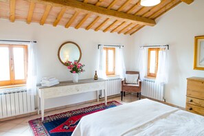 Quarto com cama, escrivaninha de madeira, cadeira, cômoda e janela com cortinas.