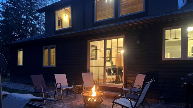 Ett modernt hus med en eldstad på uteplatsen, omgiven av stolar.