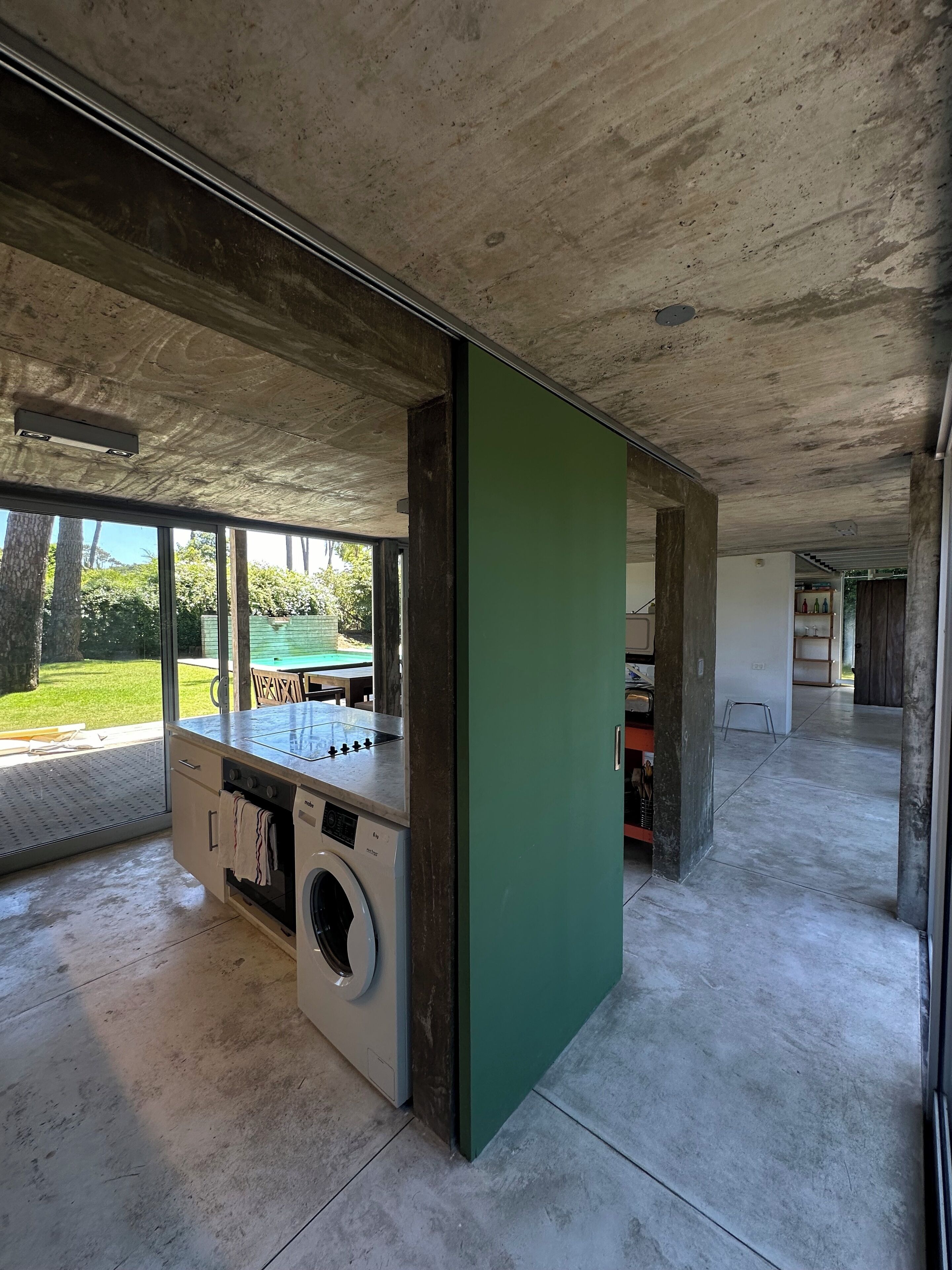 Een ruime kamer met een groot raam, een wasmachine en een groene scheidingswand.