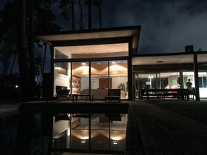 Un bâtiment moderne doté d’une façade en verre, d’un espace extérieur aménagé pour s’asseoir et d’un bassin dont la surface réfléchit la lumière.