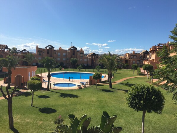 Ein Pool, umgeben von einem gepflegten Rasen, Palmen und einer Reihe mehrstöckiger Gebäude mit Balkonen.
