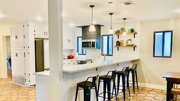 A modern kitchen with white cabinetry, a central island with bar stools, and a large window providing natural light. - Spacious lakefront home with dock - perfect for a group getaway (Lago Vista)