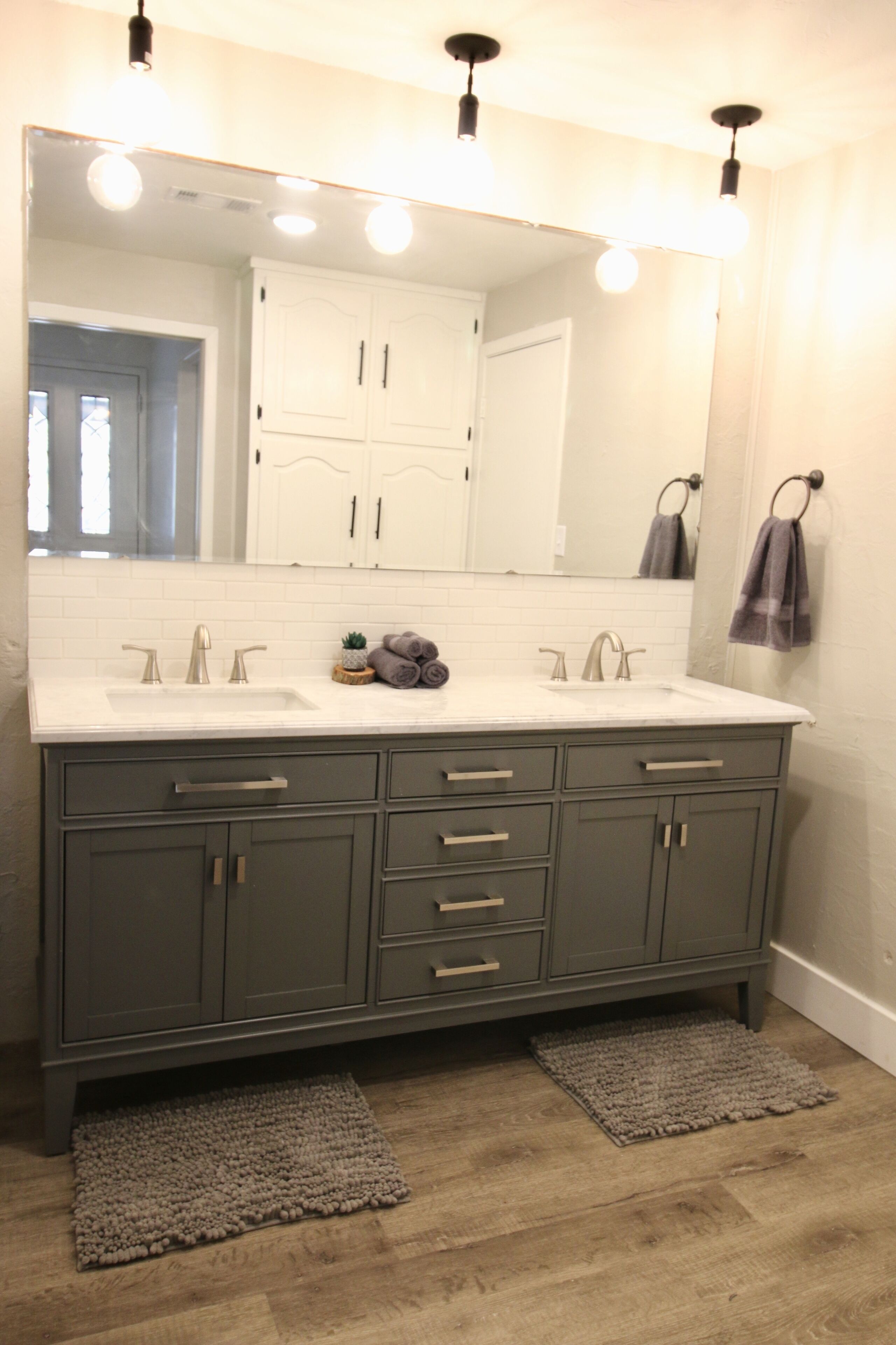 A bathroom with a white sink, two faucets, a mirror, and a dark gray cabinet with drawers.