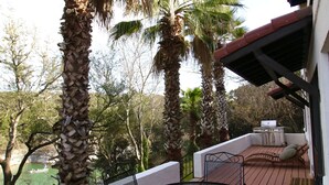A patio with a round metal table and chairs, surrounded by palm trees and a view of a body of water. - Spacious lakefront home with dock - perfect for a group getaway (Lago Vista)