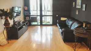 A modern living room with a black leather sofa, a TV, a bookshelf, and a large window. - Family Apt ❤️ underground parking❤️smoking balcony (Sector 2)