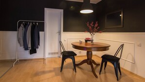 A room with a round wooden table, two black chairs, a hanging light fixture, a coat rack with several jackets, and a vase with red berries on a small table. - Family Apt ❤️ underground parking❤️smoking balcony (Sector 2)