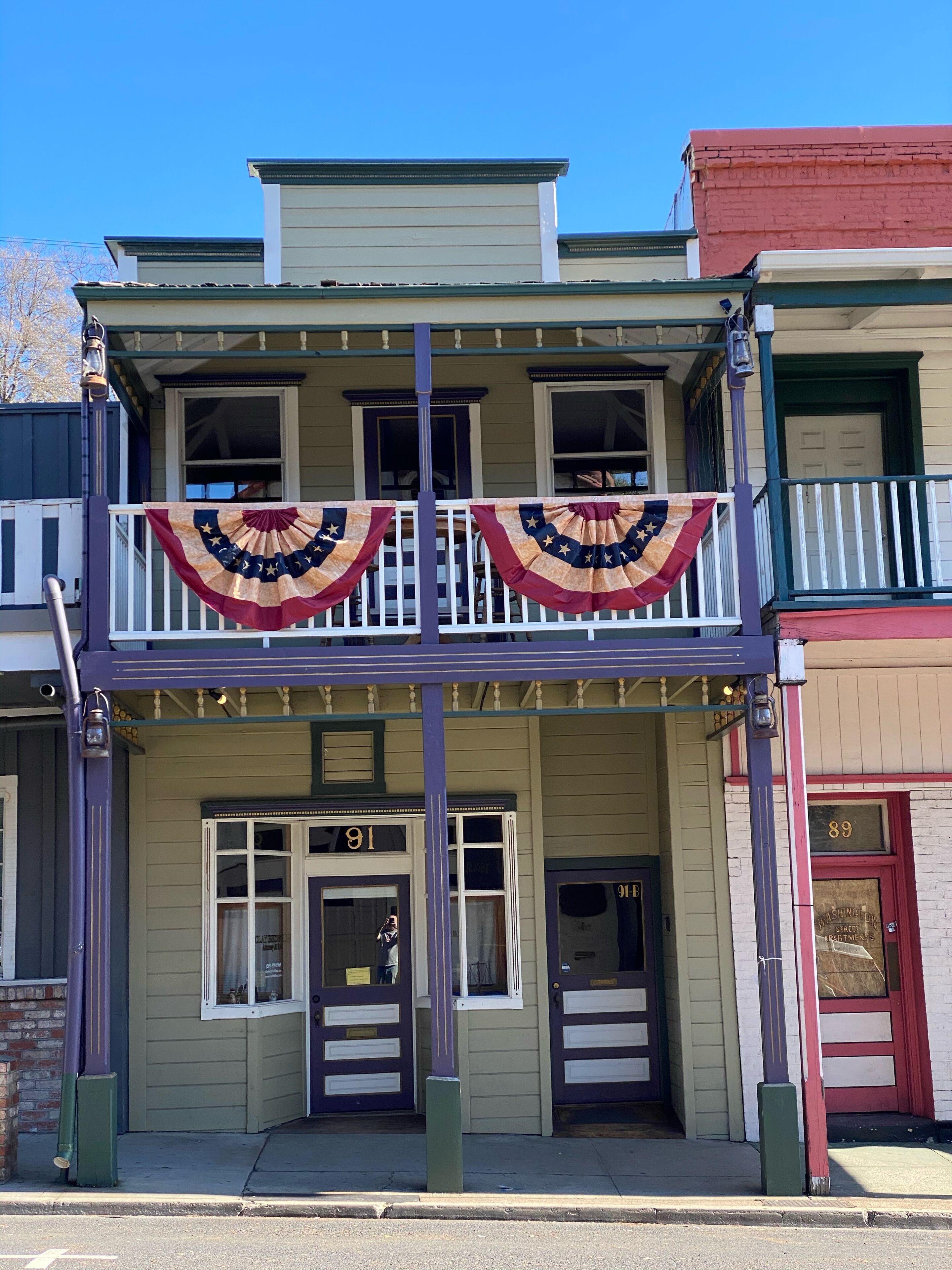 A two-story building with a balcony, numbered 91, featuring a traditional facade with a flat roof and a red door.