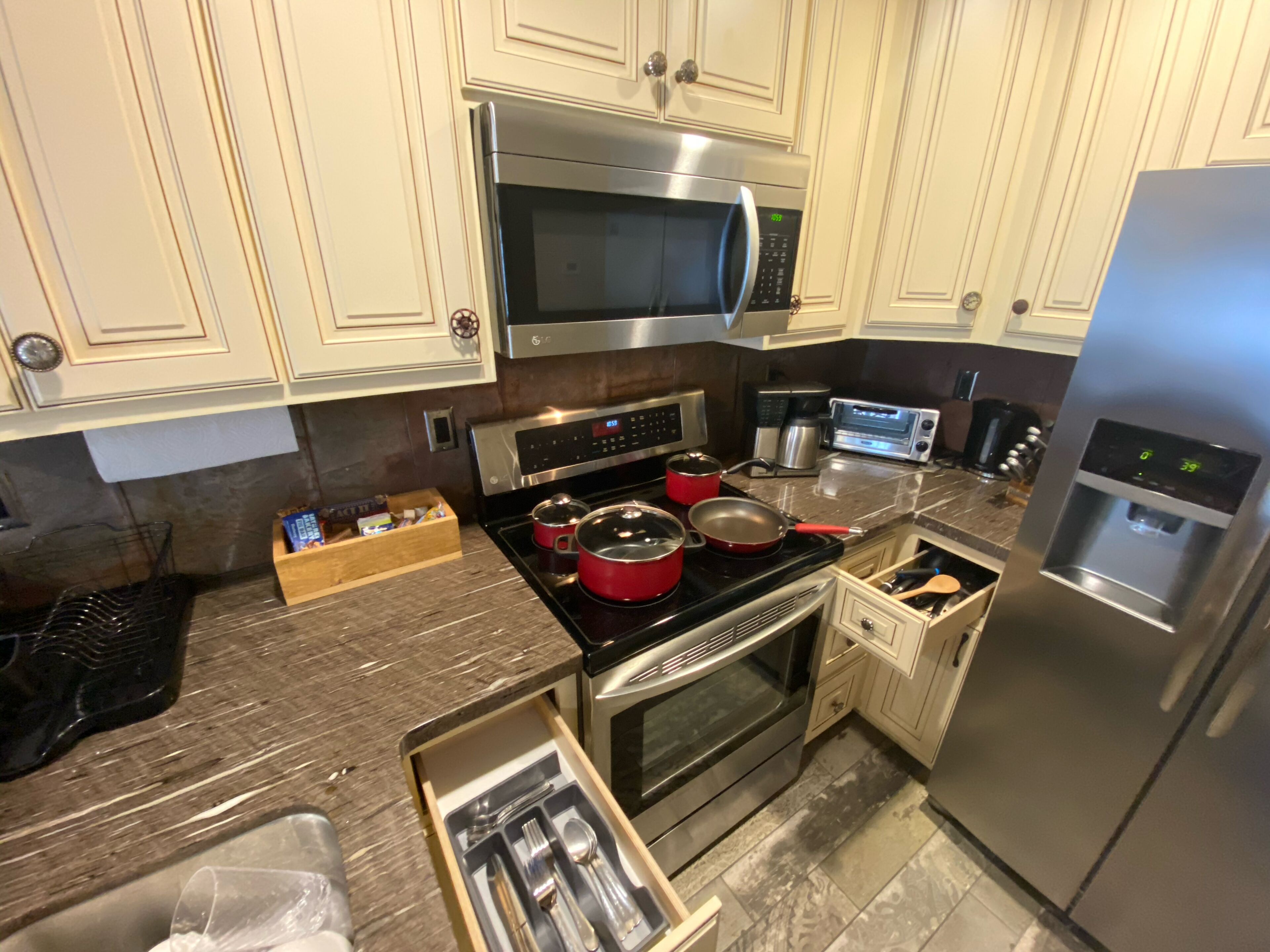 A modern kitchen with stainless steel appliances, including a microwave, oven, and refrigerator. There is a wooden countertop with a drawer containing utensils.