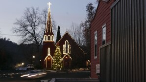 Uma igreja com uma torre alta e luzes de Natal, um edifício vermelho com um campanário e uma cerca de metal.
