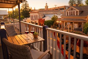 A wooden table with two wine glasses and a potted plant on a balcony with a railing.