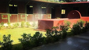 A building with a covered outdoor area, a paved path, and small shrubs along the edge. - Le Vecchie Scuderie (Fara in Sabina)