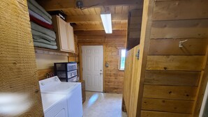 A laundry room with a washing machine, a dryer, and neatly stacked linens on shelves. - Bear Cabin in the Heart of Moose Country Alaska! (Ninilchik)