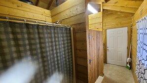A wooden interior with a checkered shower curtain, a door, and a broom leaning against the wall. - Bear Cabin in the Heart of Moose Country Alaska! (Ninilchik)