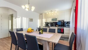 Une cuisine moderne avec des meubles blancs, un four à micro-ondes et une cuisinière. On y trouve une table à manger avec des chaises et un panier de fruits.