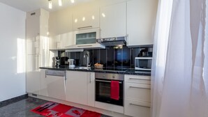 Une cuisine moderne avec des armoires blanches, un plan de travail noir, un four encastré et un four à micro-ondes.