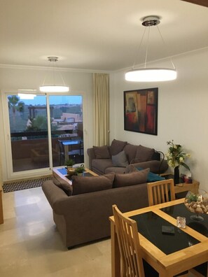 Una sala moderna con un sofá modular, una mesa de comedor con sillas, un ventanal con vistas al exterior y un ventilador de techo.