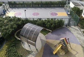 Una cancha de baloncesto al aire libre con zona de estar cubierta y un tobogán.